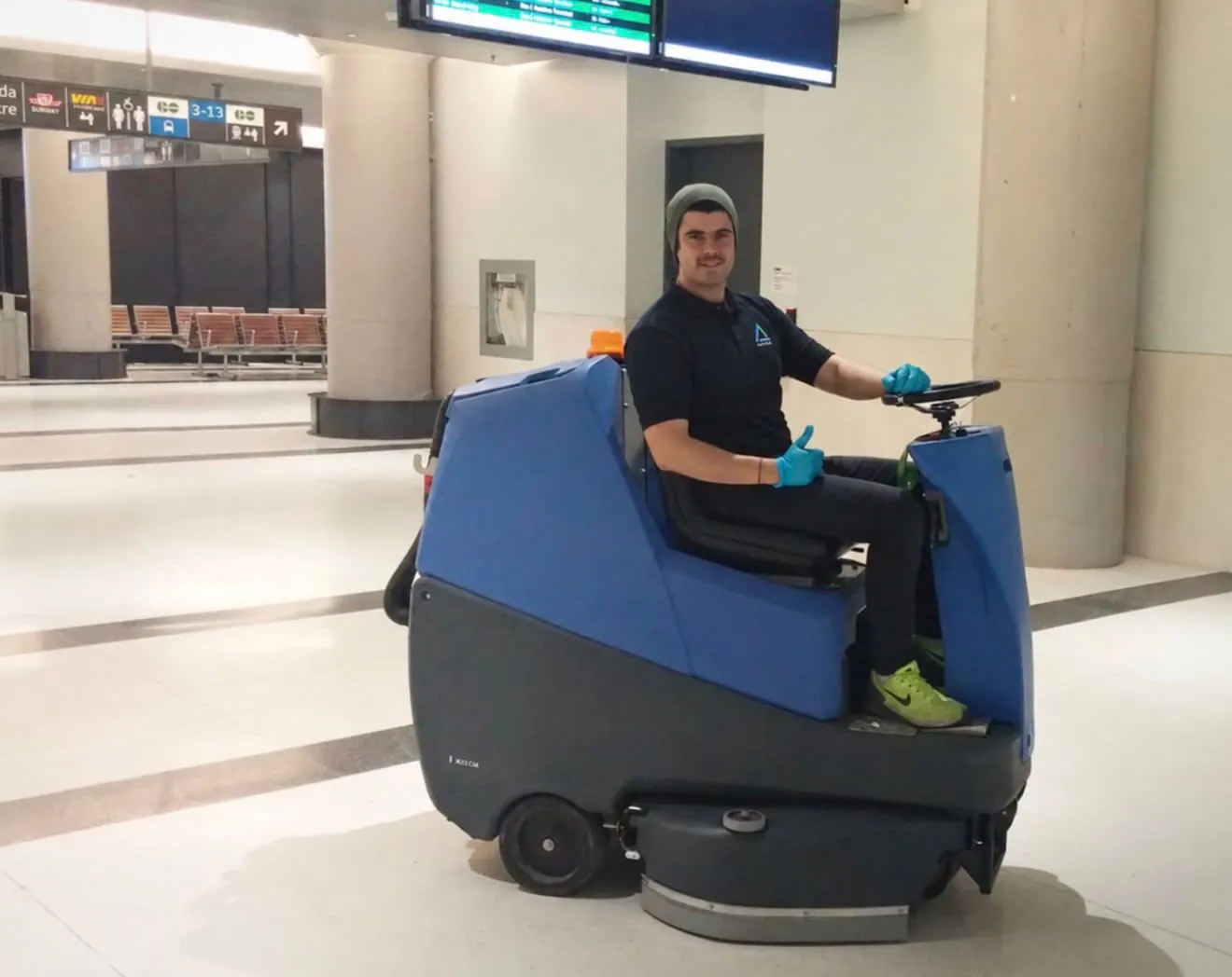 A ride-on floor scrubber cleaning a large commercial hall